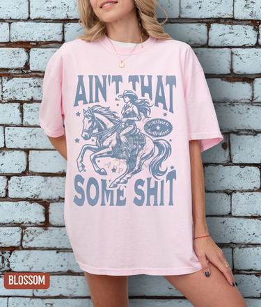 A woman wearing a pink t-shirt with a graphic design of a cowboy riding a horse and the text